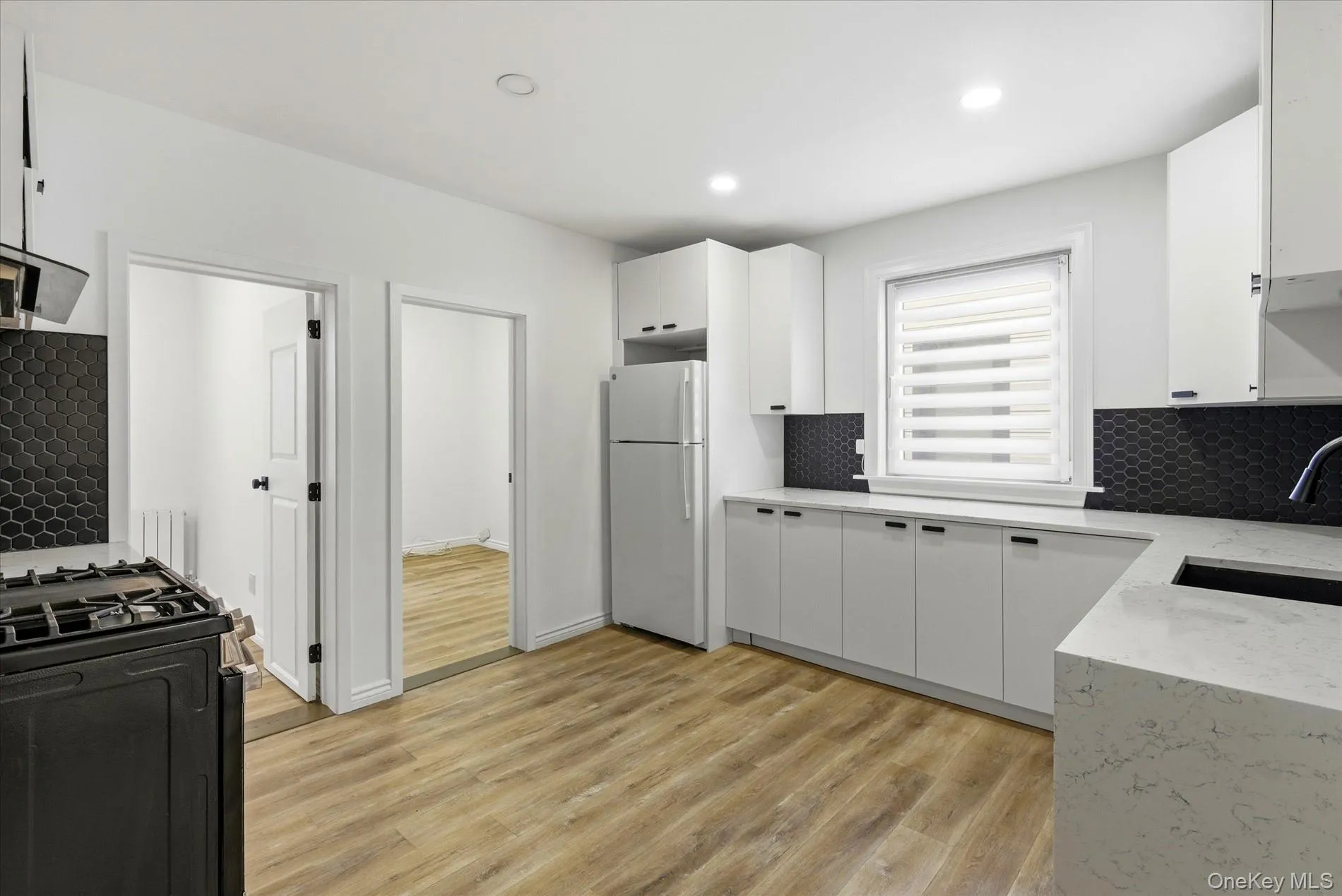 Kitchen with light stone counters, white cabinets, freestanding refrigerator, light wood-style floors, and decorative backsplash Kitchen with light stone counters, white cabinets, freestanding refrigerator, light wood-style floors, and decorative backsplash