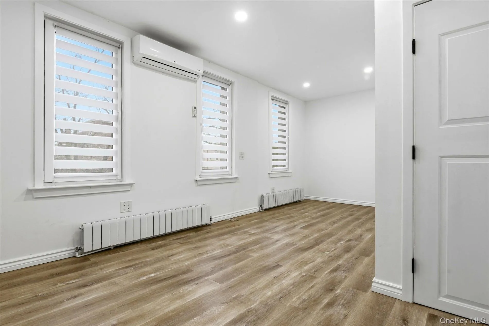 Empty room featuring radiator heating unit, light wood finished floors, a wall unit AC, and recessed lighting Empty room featuring radiator heating unit, light wood finished floors, a wall unit AC, and recessed lighting