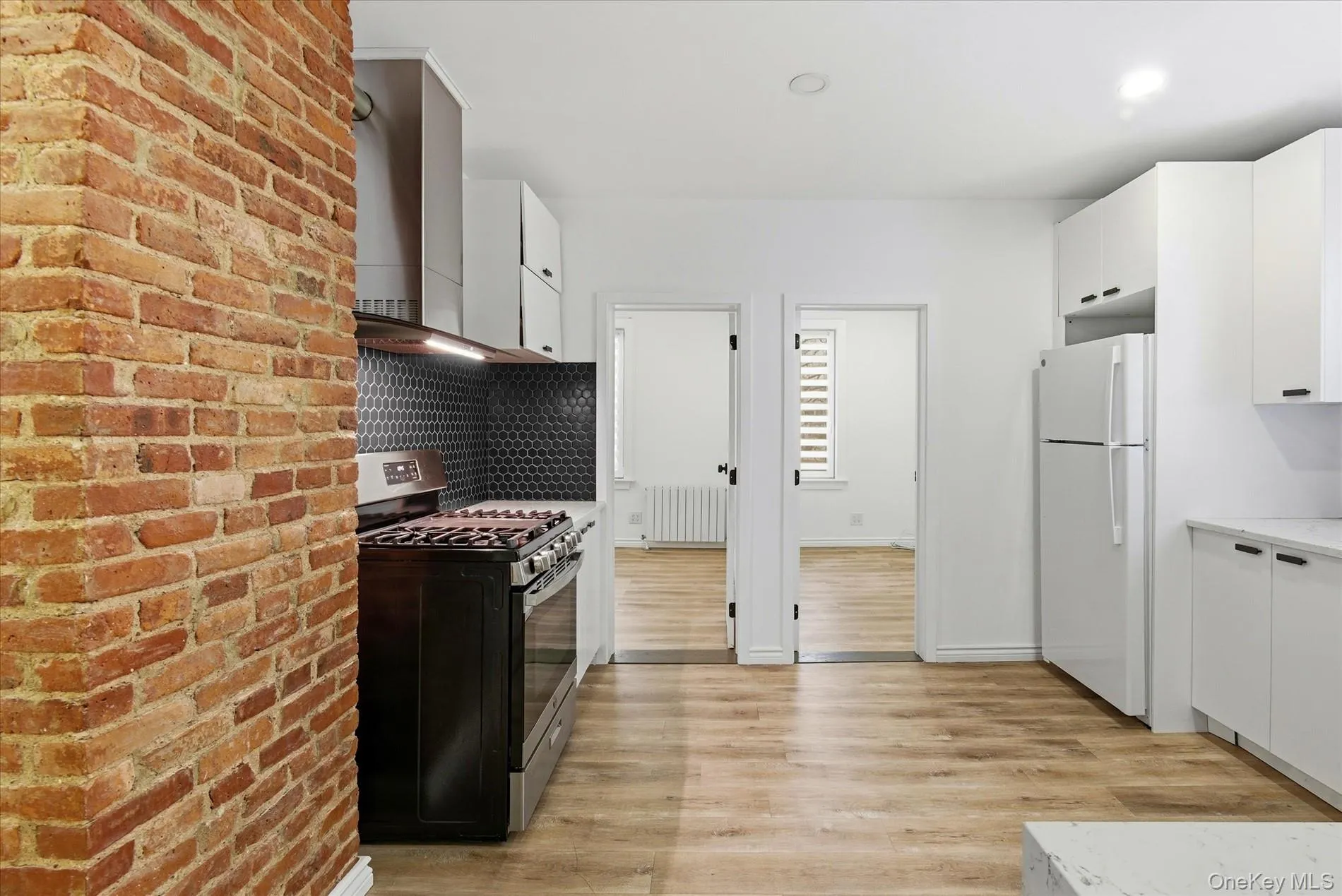 Kitchen featuring gas range, white cabinetry, radiator heating unit, freestanding refrigerator, and light wood-type flooring Kitchen featuring gas range, white cabinetry, radiator heating unit, freestanding refrigerator, and light wood-type flooring