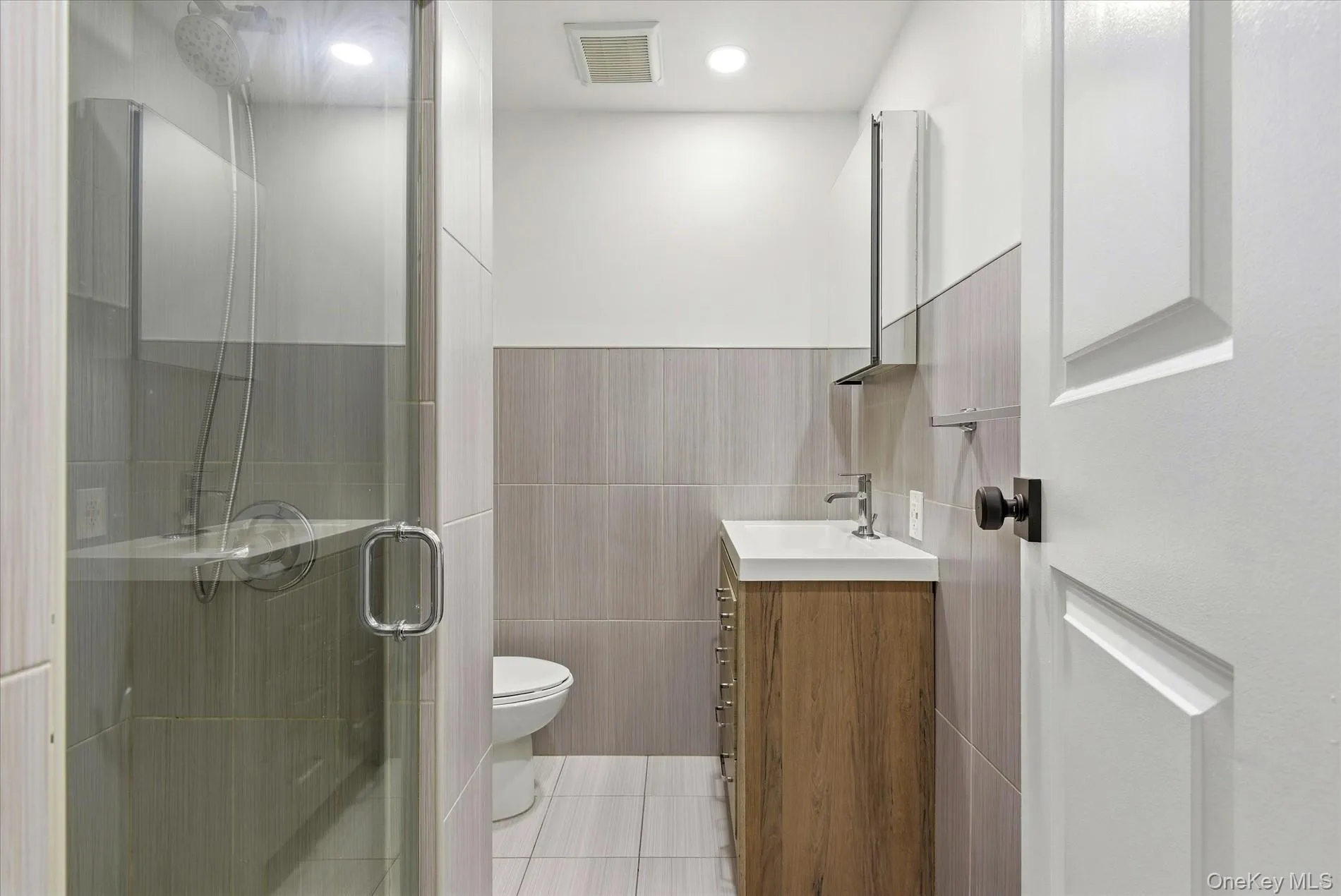 Full bath featuring vanity, a shower stall, tile walls, light tile patterned flooring, and recessed lighting Full bath featuring vanity, a shower stall, tile walls, light tile patterned flooring, and recessed lighting