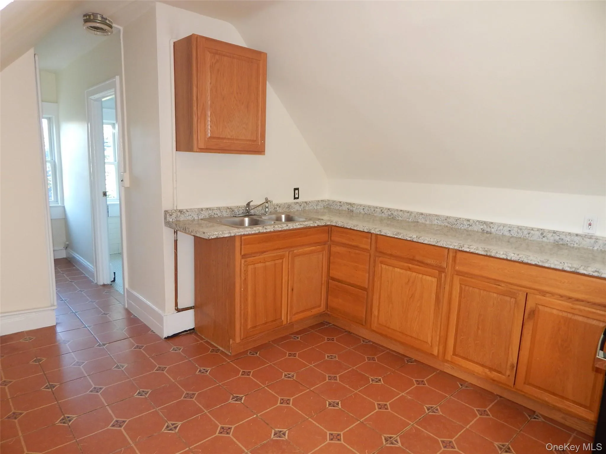 Kitchen with lofted ceiling, brown cabinets, light countertops, and dark tile patterned flooring Kitchen with lofted ceiling, brown cabinets, light countertops, and dark tile patterned flooring