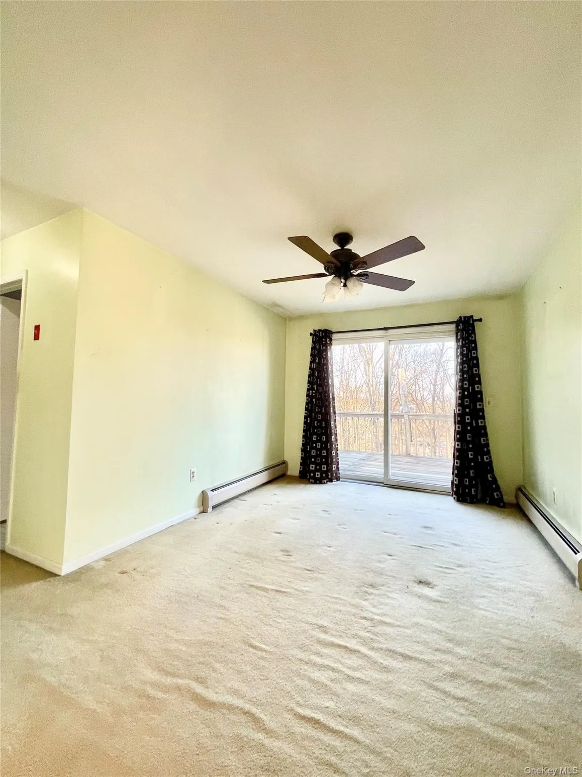 Empty room featuring a baseboard radiator, light carpet, and ceiling fan Empty room featuring a baseboard radiator, light carpet, and ceiling fan