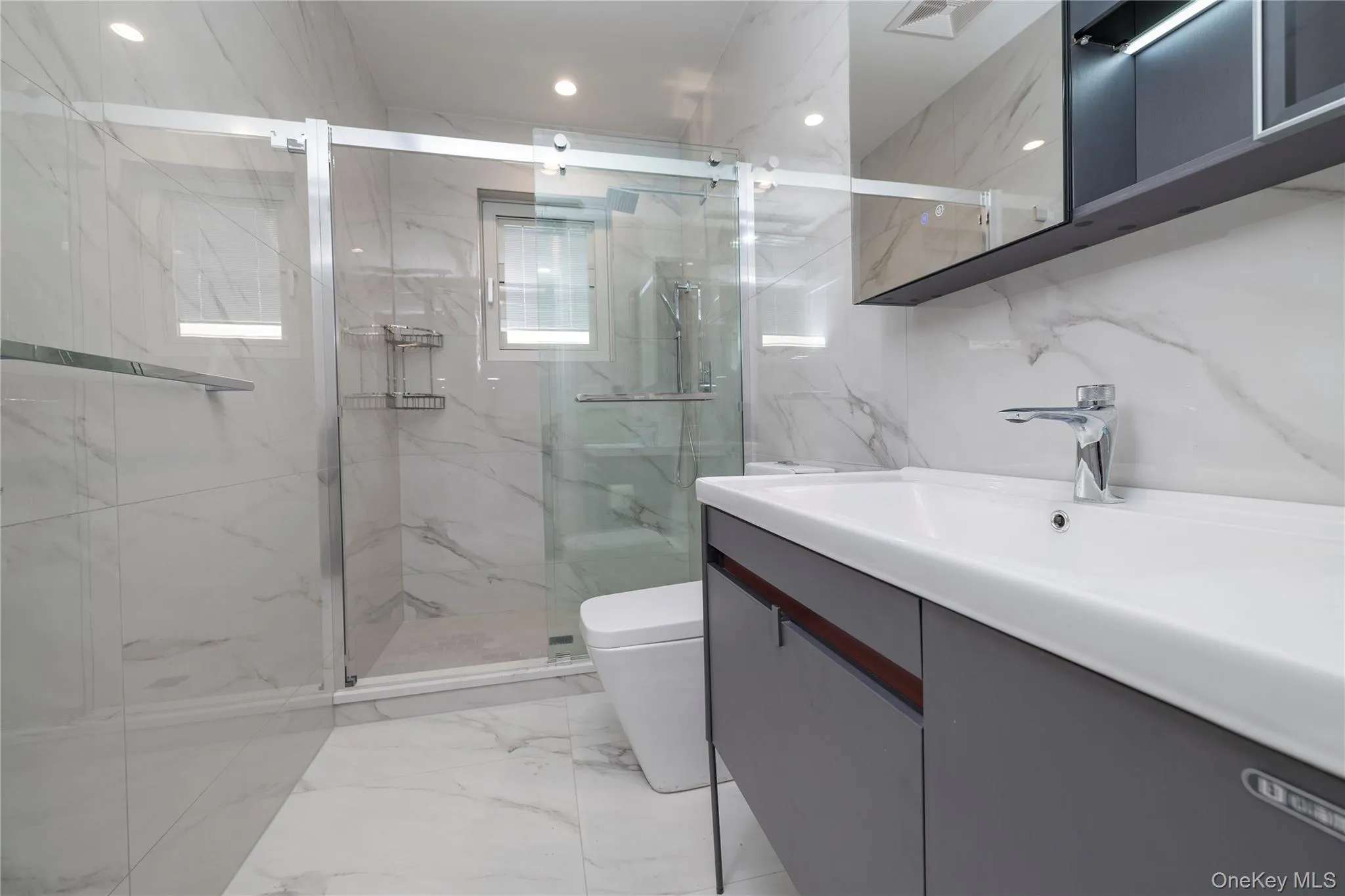 Bathroom with light marble finish floors, vanity, a marble finish shower, stone wall, and tile walls Bathroom with light marble finish floors, vanity, a marble finish shower, stone wall, and tile walls