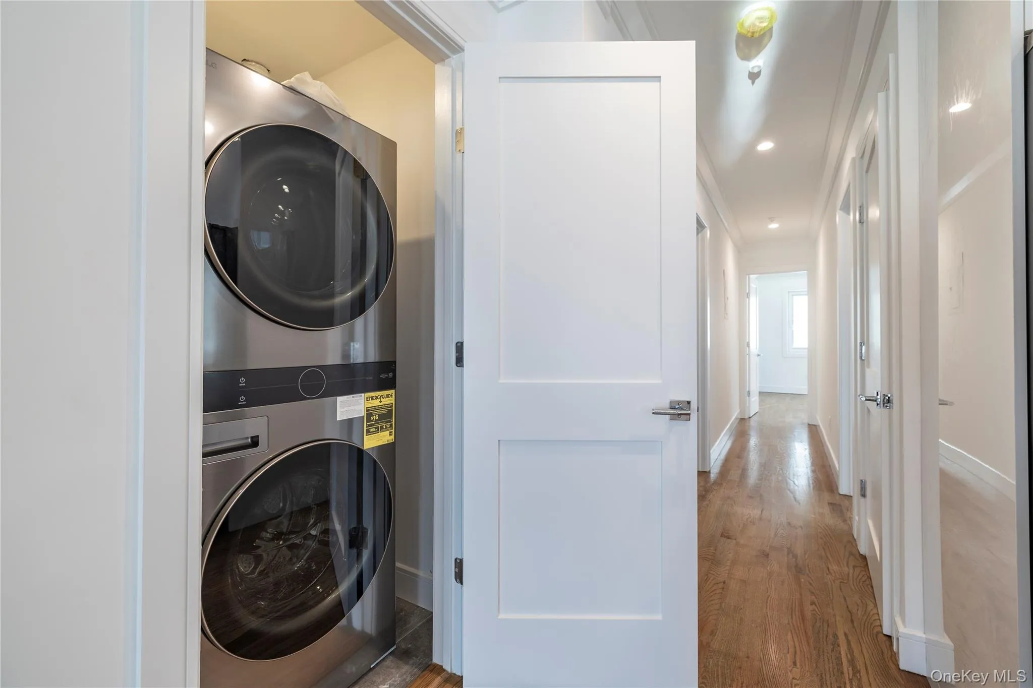 Laundry area featuring stacked washing machine and dryer, wood finished floors, recessed lighting, and ornamental molding Laundry area featuring stacked washing machine and dryer, wood finished floors, recessed lighting, and ornamental molding