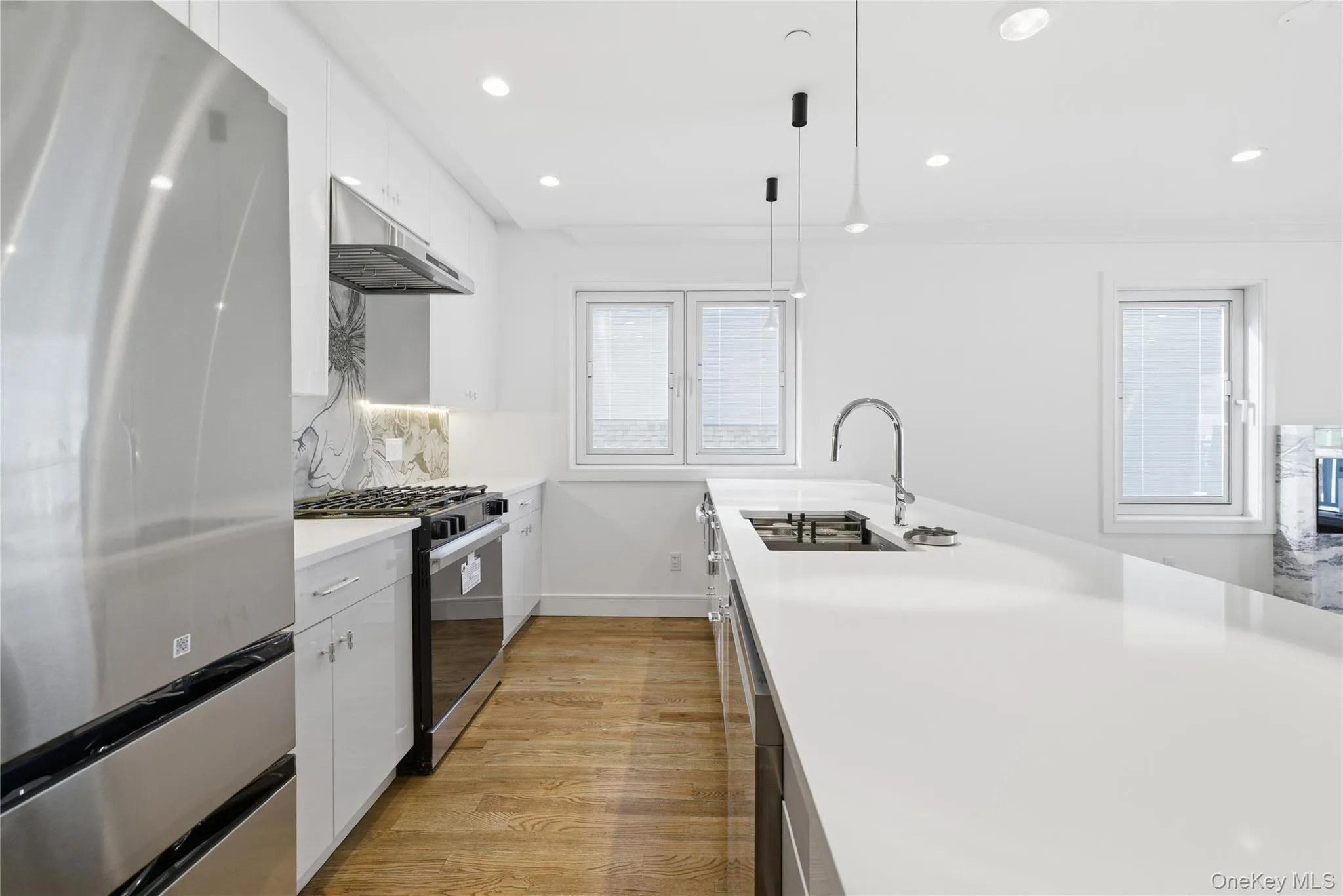 Kitchen featuring appliances with stainless steel finishes, white cabinets, hanging light fixtures, light wood finished floors, and recessed lighting Kitchen featuring appliances with stainless steel finishes, white cabinets, hanging light fixtures, light wood finished floors, and recessed lighting