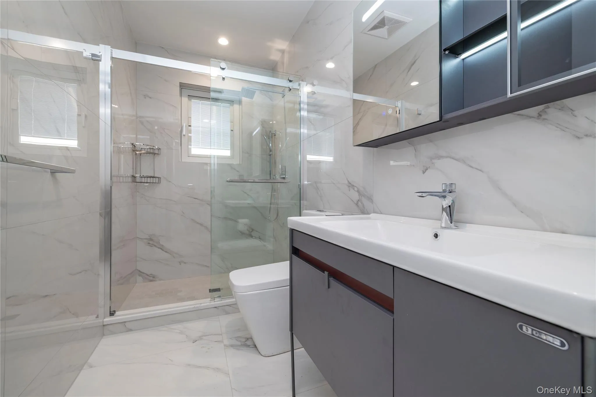 Bathroom with light marble finish flooring, vanity, a marble finish shower, stone wall, and tile walls Bathroom with light marble finish flooring, vanity, a marble finish shower, stone wall, and tile walls