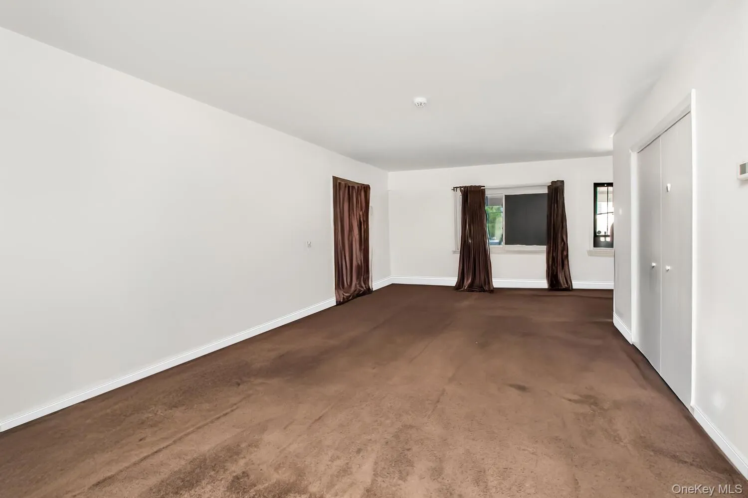 Empty room featuring baseboards and dark colored carpet Empty room featuring baseboards and dark colored carpet