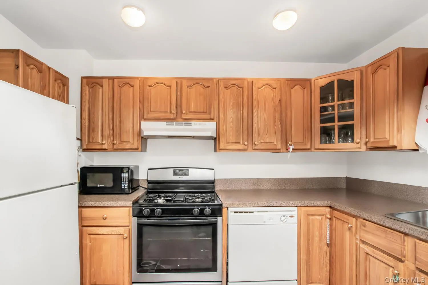 Kitchen with white appliances, under cabinet range hood, glass insert cabinets, and brown cabinets Kitchen with white appliances, under cabinet range hood, glass insert cabinets, and brown cabinets