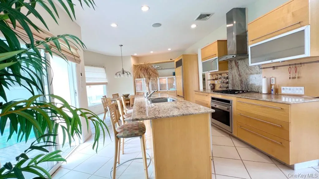 Kitchen with a kitchen island with sink, tasteful backsplash, exhaust hood, decorative light fixtures, and light stone countertops Kitchen with a kitchen island with sink, tasteful backsplash, exhaust hood, decorative light fixtures, and light stone countertops