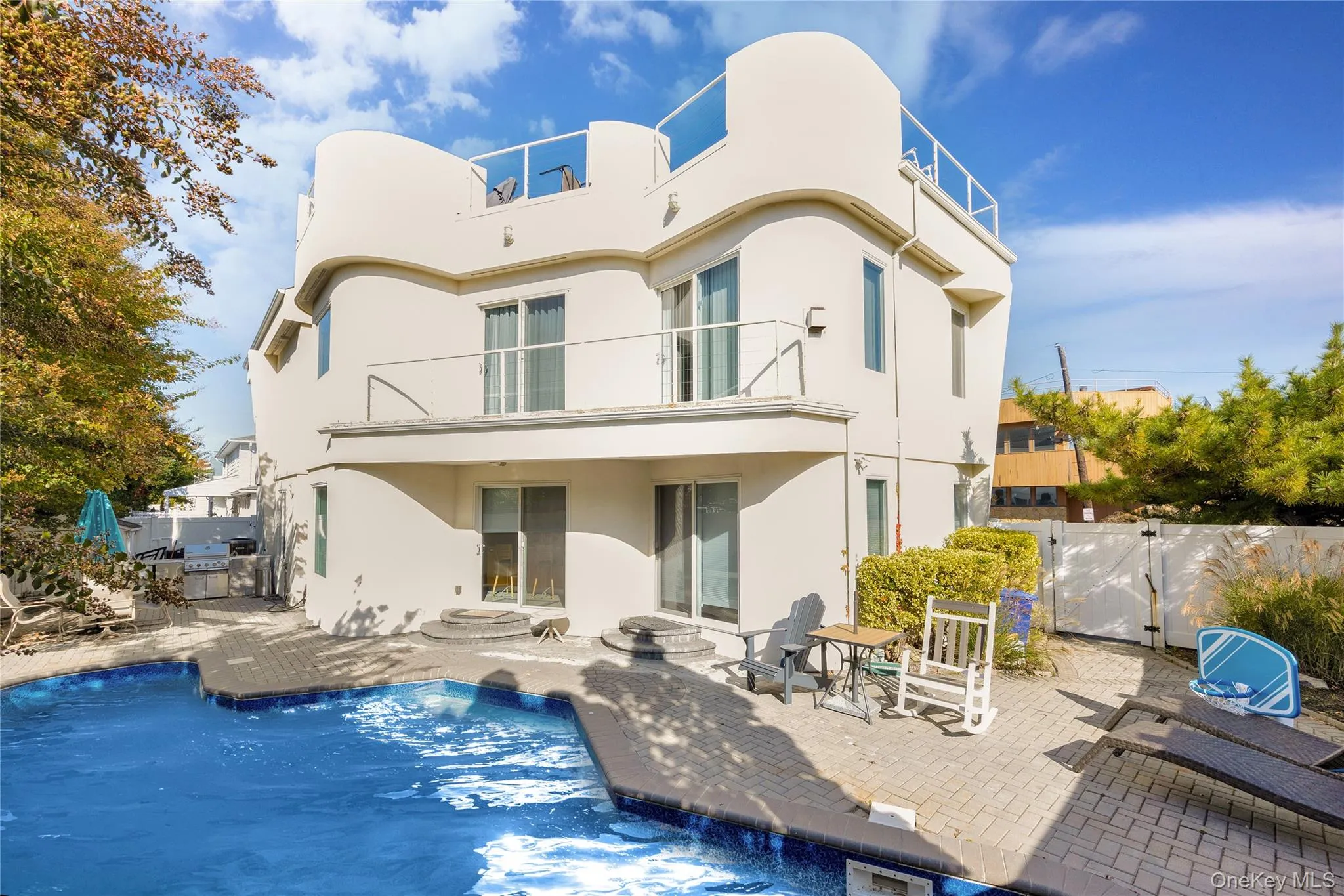 Back of house with a gate, a balcony, a patio area, and stucco siding Back of house with a gate, a balcony, a patio area, and stucco siding