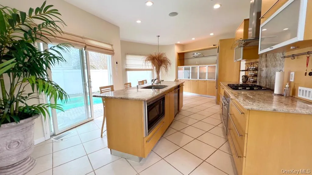 Kitchen with light stone countertops, a kitchen island with sink, ventilation hood, a kitchen breakfast bar, and stainless steel appliances Kitchen with light stone countertops, a kitchen island with sink, ventilation hood, a kitchen breakfast bar, and stainless steel appliances