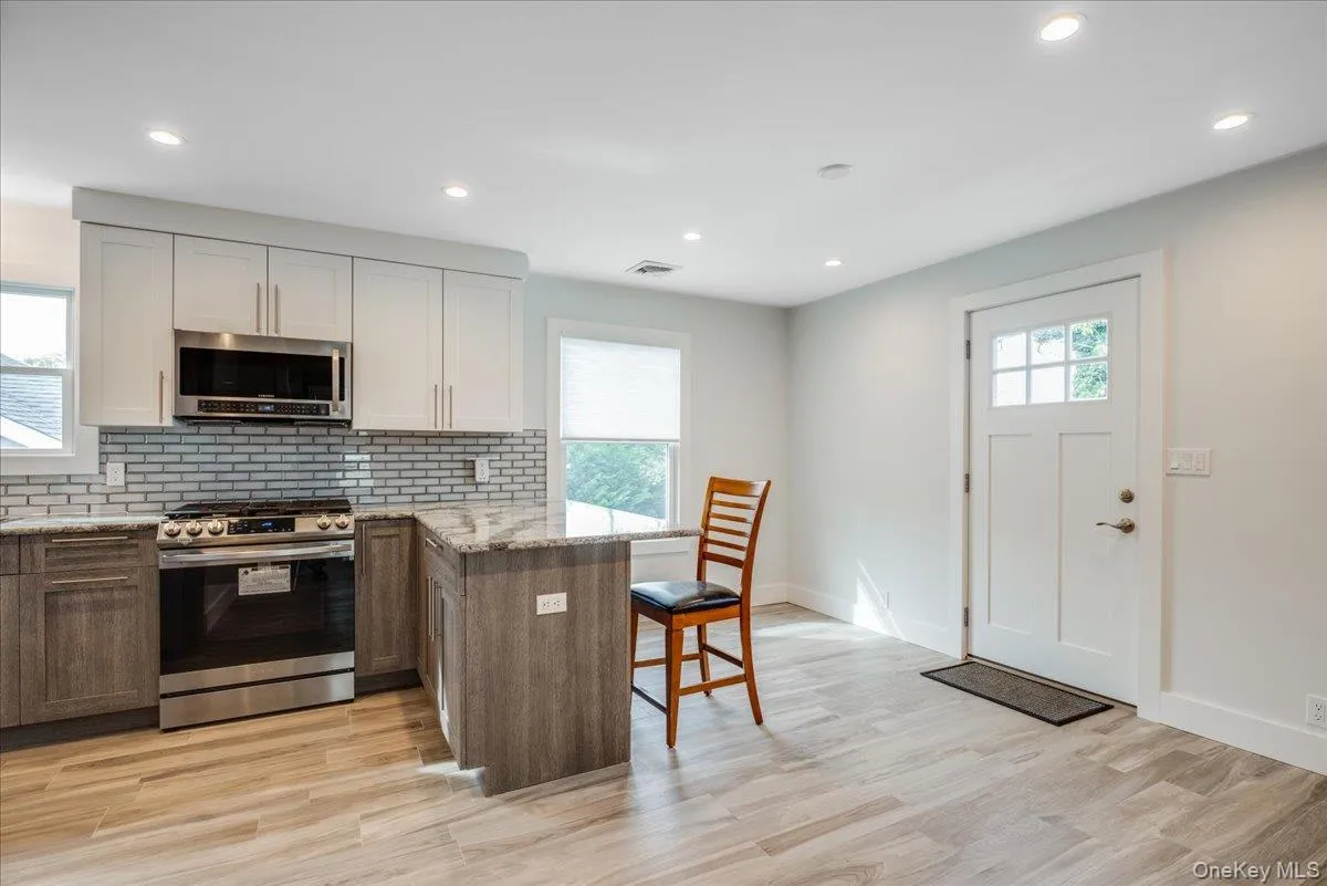 Kitchen featuring a peninsula, stainless steel appliances, tasteful backsplash, white cabinetry, and light stone countertops Kitchen featuring a peninsula, stainless steel appliances, tasteful backsplash, white cabinetry, and light stone countertops