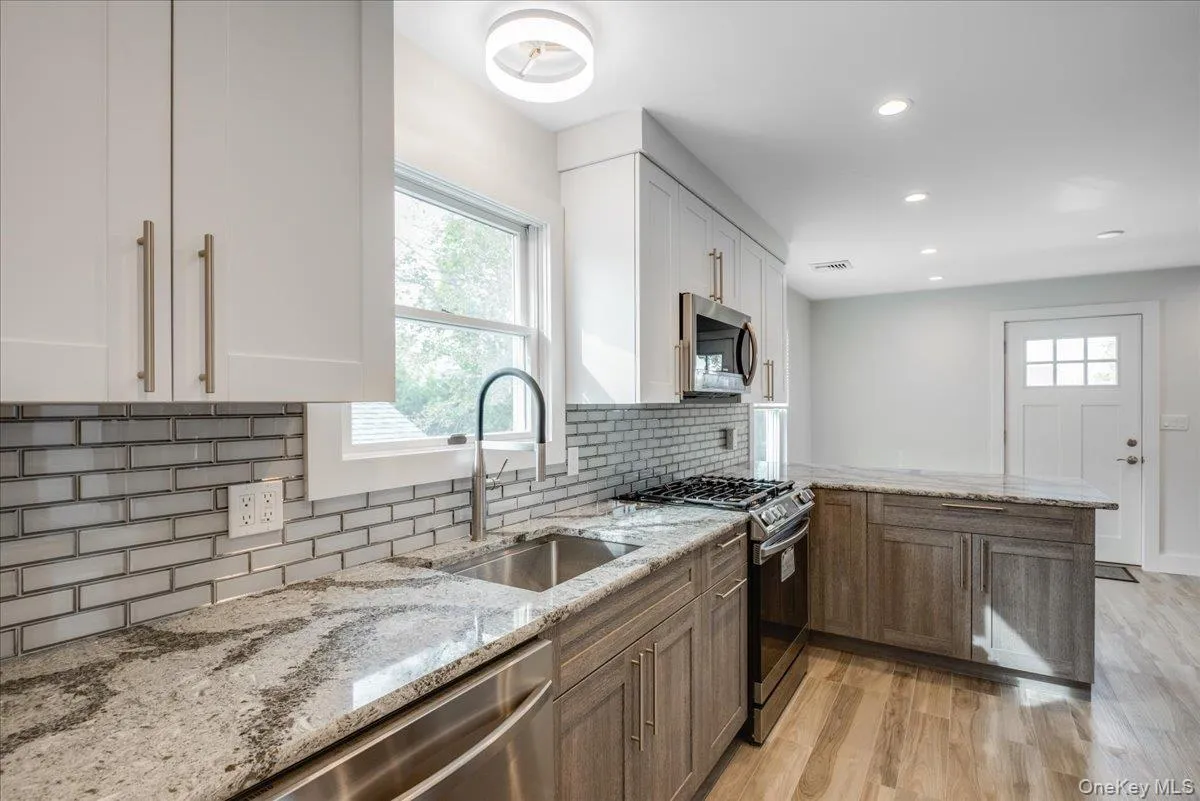 Kitchen featuring appliances with stainless steel finishes, light stone countertops, a peninsula, light wood finished floors, and white cabinets Kitchen featuring appliances with stainless steel finishes, light stone countertops, a peninsula, light wood finished floors, and white cabinets