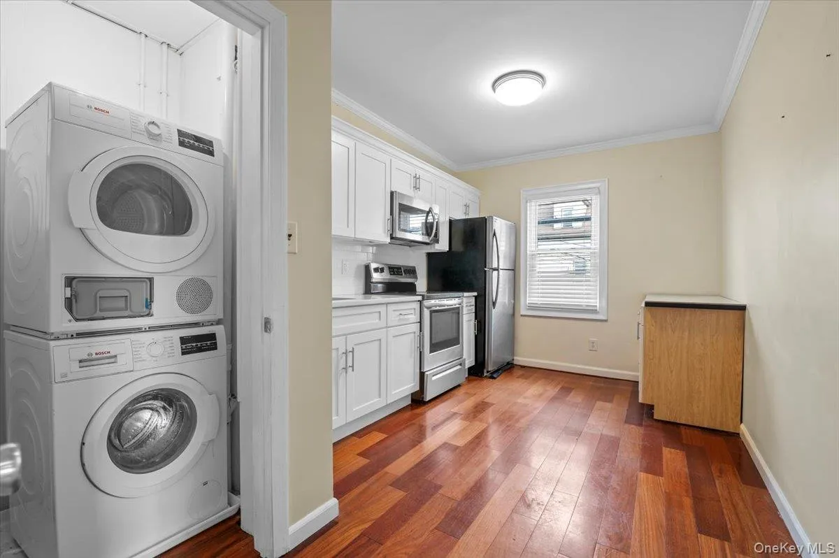 Washroom featuring stacked washing machine and dryer, dark wood-type flooring, and crown molding Washroom featuring stacked washing machine and dryer, dark wood-type flooring, and crown molding