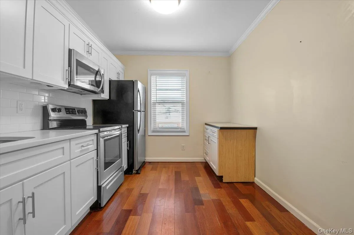 Kitchen with white cabinetry, stainless steel appliances, dark wood finished floors, crown molding, and tasteful backsplash Kitchen with white cabinetry, stainless steel appliances, dark wood finished floors, crown molding, and tasteful backsplash