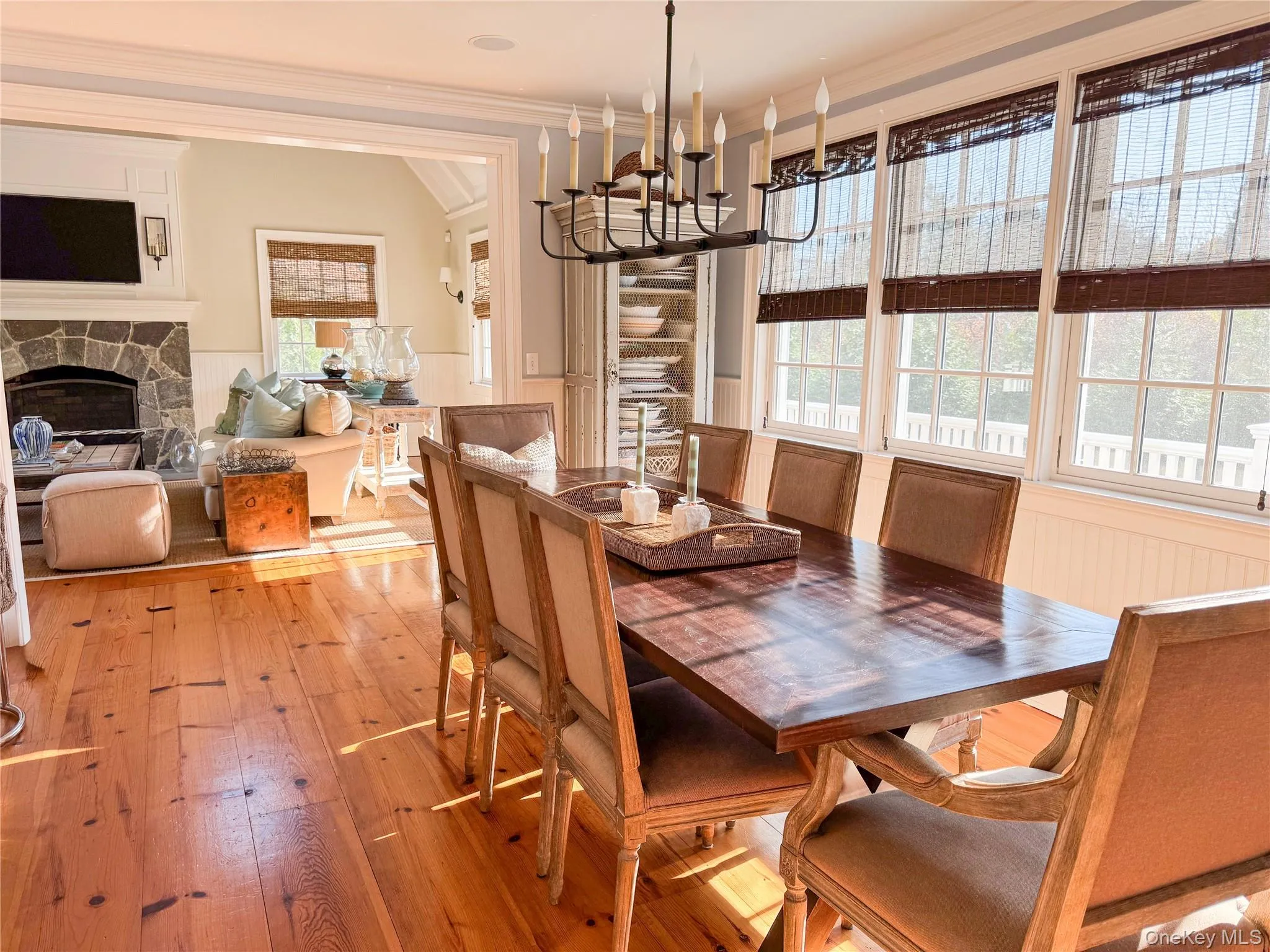 Dining space featuring crown molding, wainscoting, a stone fireplace, wood-type flooring, and a chandelier Dining space featuring crown molding, wainscoting, a stone fireplace, wood-type flooring, and a chandelier