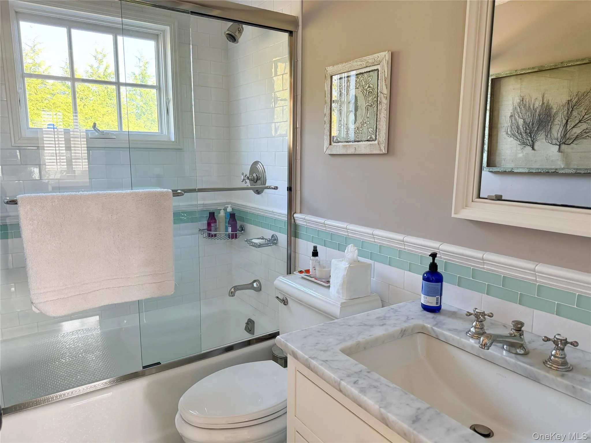 Bathroom featuring vanity, shower / bath combination with glass door, tile walls, and wainscoting Bathroom featuring vanity, shower / bath combination with glass door, tile walls, and wainscoting