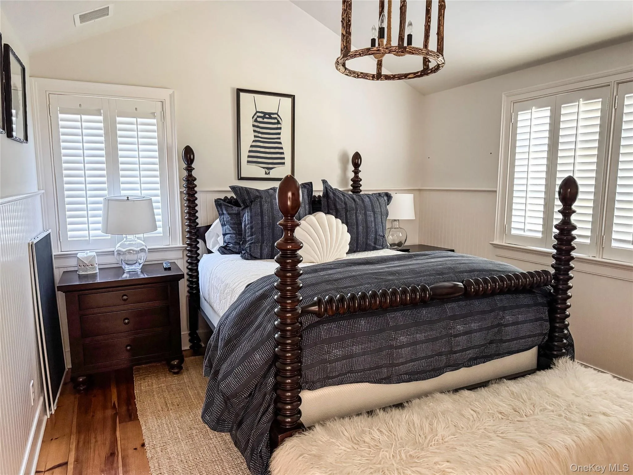Bedroom featuring wainscoting, lofted ceiling, wood finished floors, multiple windows, and a decorative wall Bedroom featuring wainscoting, lofted ceiling, wood finished floors, multiple windows, and a decorative wall