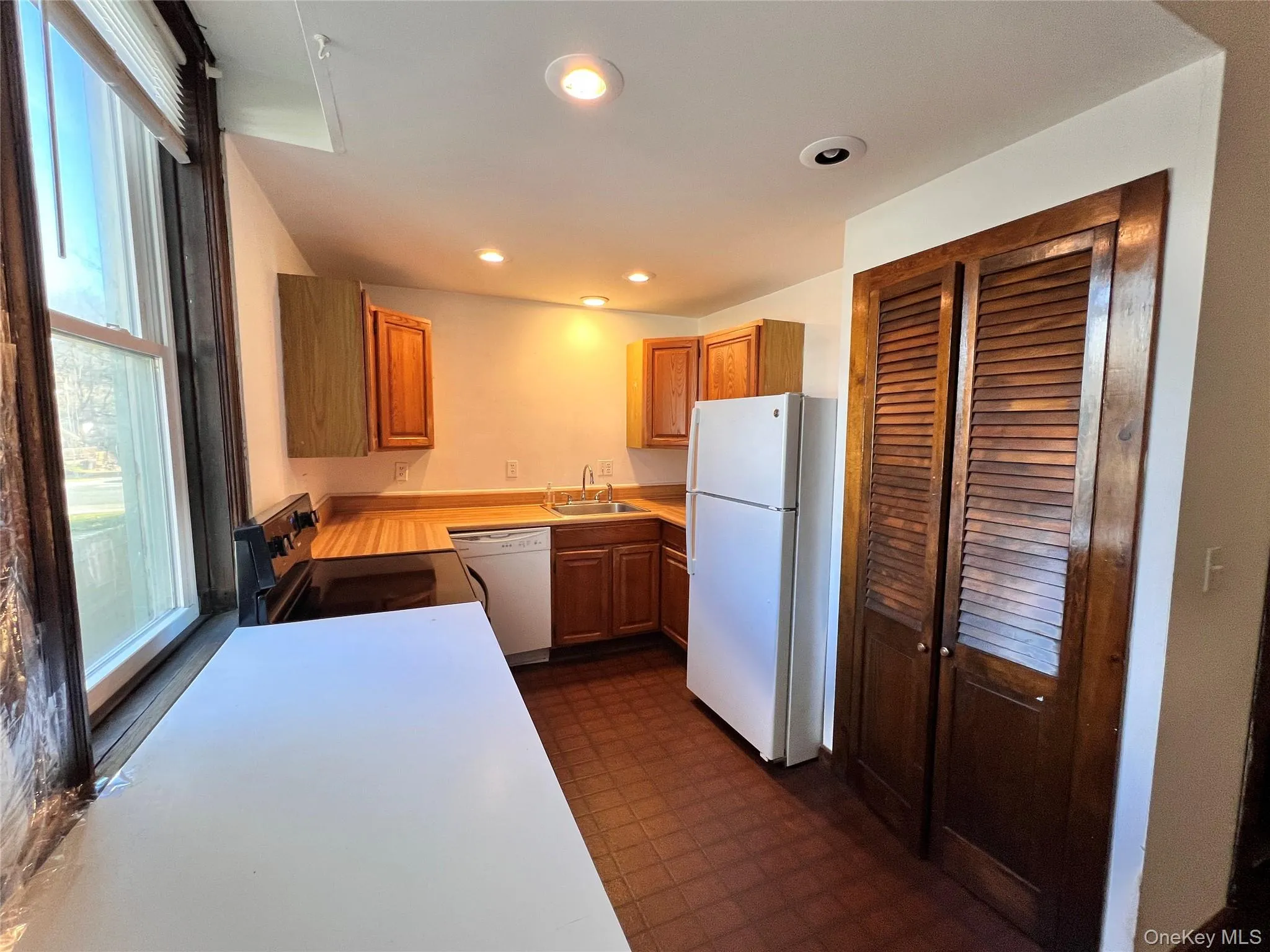 Kitchen featuring dark floors, white appliances, light countertops, recessed lighting, and brown cabinets Kitchen featuring dark floors, white appliances, light countertops, recessed lighting, and brown cabinets
