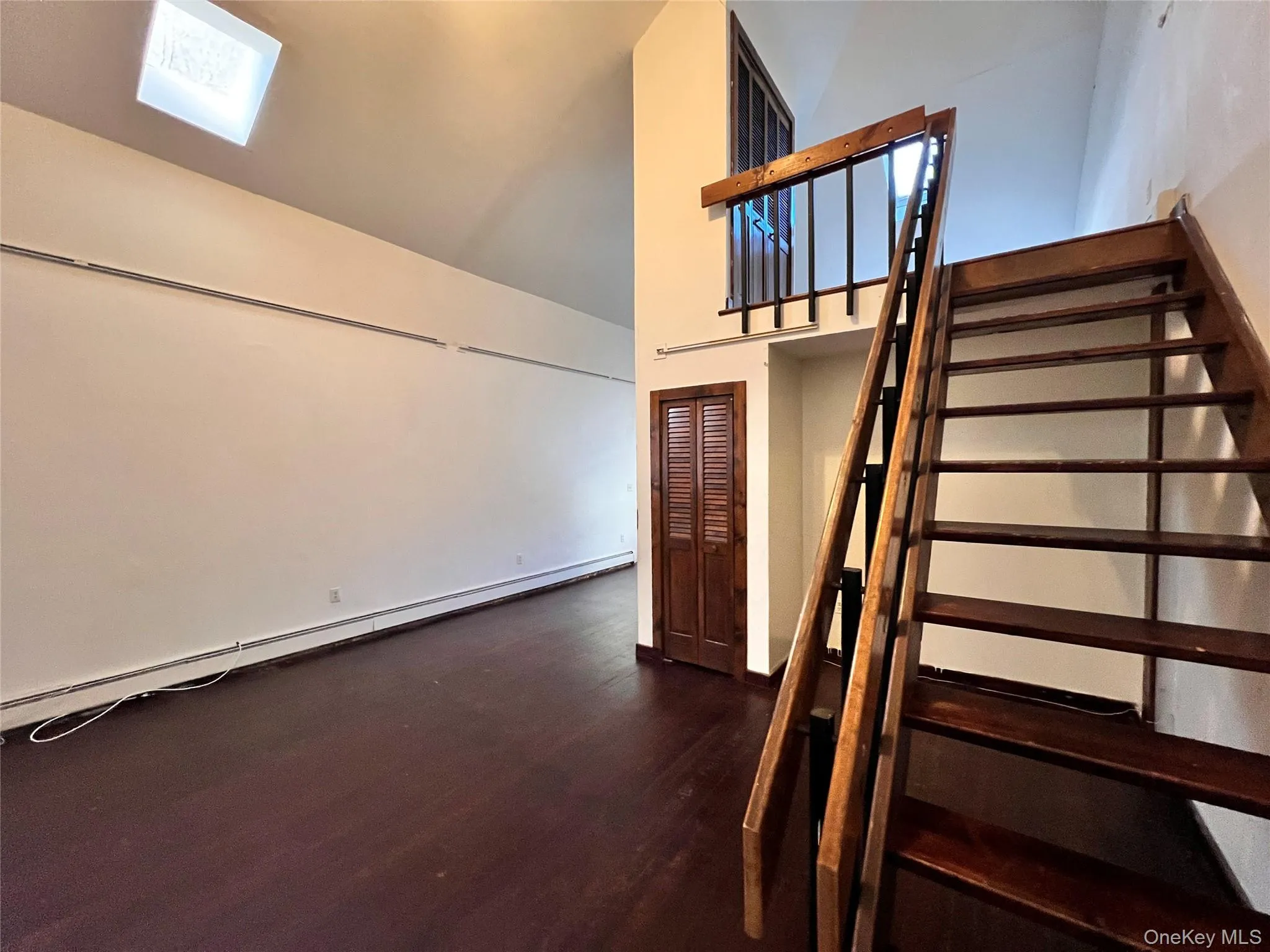 Staircase featuring a baseboard heating unit, a towering ceiling, and wood finished floors Staircase featuring a baseboard heating unit, a towering ceiling, and wood finished floors