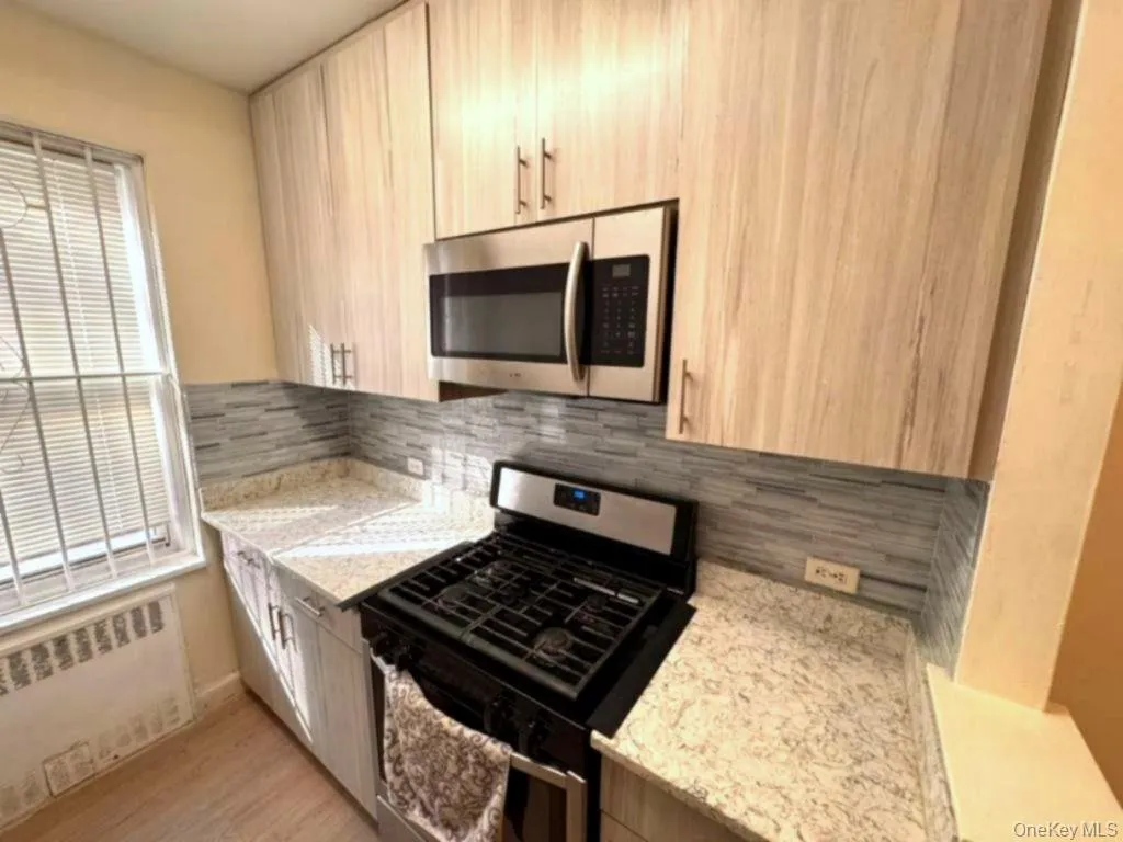 Kitchen featuring stainless steel appliances, radiator heating unit, light stone counters, and backsplash Kitchen featuring stainless steel appliances, radiator heating unit, light stone counters, and backsplash