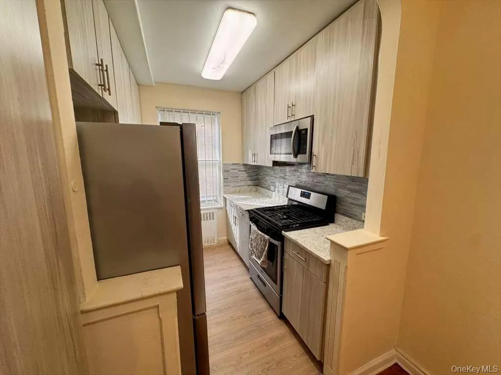 Kitchen featuring stainless steel appliances, light stone counters, light wood-type flooring, and light brown cabinetry Kitchen featuring stainless steel appliances, light stone counters, light wood-type flooring, and light brown cabinetry