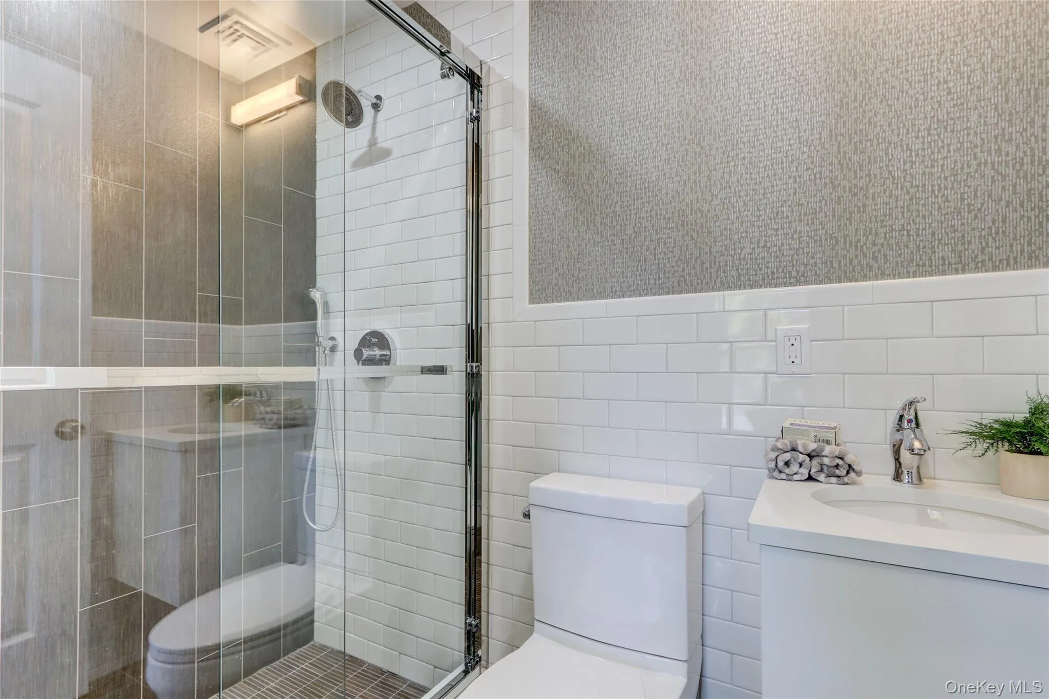 Bathroom with wallpapered walls, tile walls, vanity, a stall shower, and a wainscoted wall Bathroom with wallpapered walls, tile walls, vanity, a stall shower, and a wainscoted wall