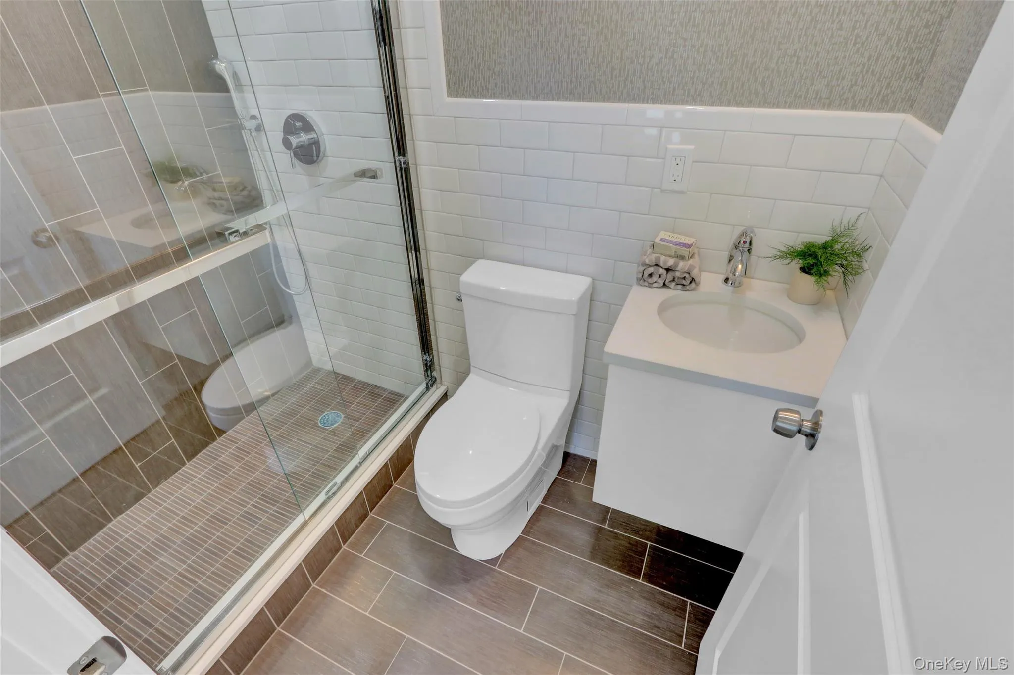 Full bathroom with vanity, tile walls, a stall shower, wallpapered walls, and a wainscoted wall Full bathroom with vanity, tile walls, a stall shower, wallpapered walls, and a wainscoted wall