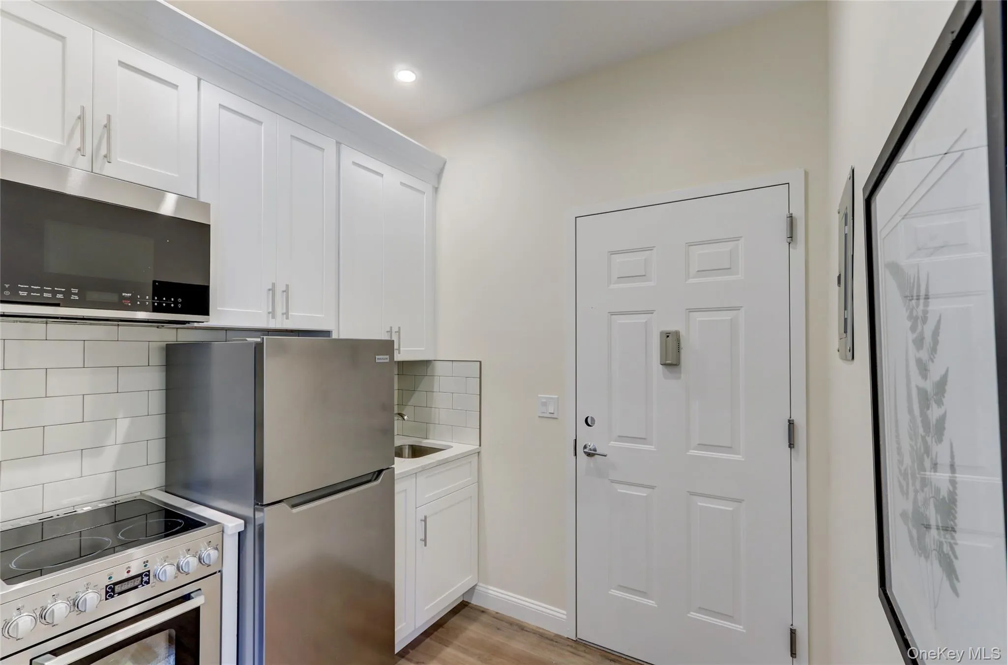 Kitchen featuring range with electric cooktop, white cabinetry, tasteful backsplash, stainless steel microwave, and light wood-style floors Kitchen featuring range with electric cooktop, white cabinetry, tasteful backsplash, stainless steel microwave, and light wood-style floors