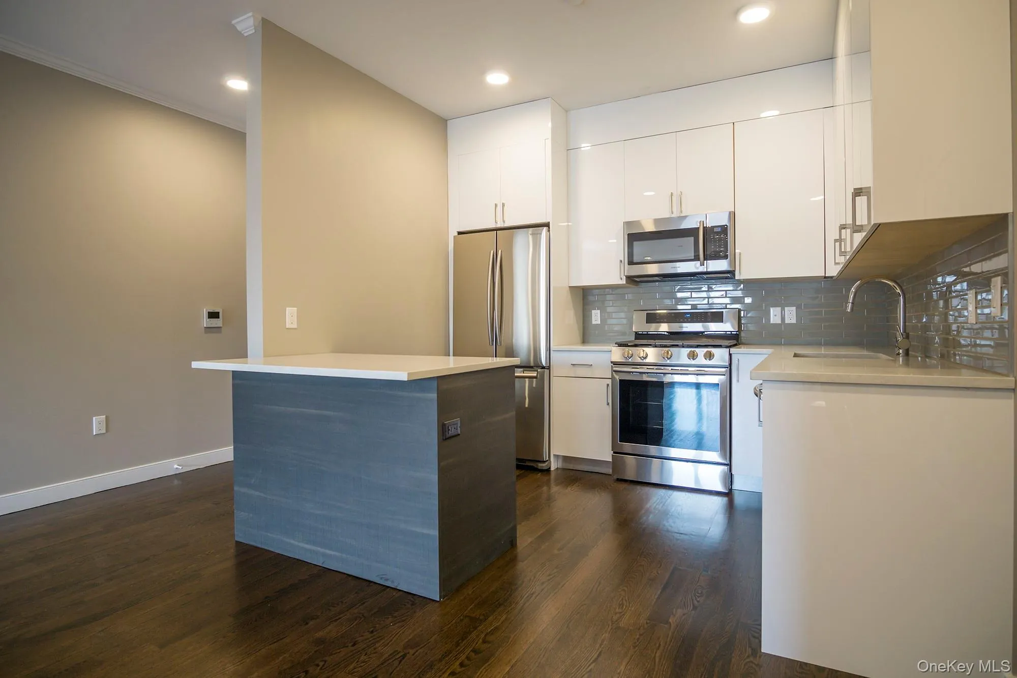 Kitchen featuring appliances with stainless steel finishes, white cabinetry, dark wood-style floors, backsplash, and a center island Kitchen featuring appliances with stainless steel finishes, white cabinetry, dark wood-style floors, backsplash, and a center island