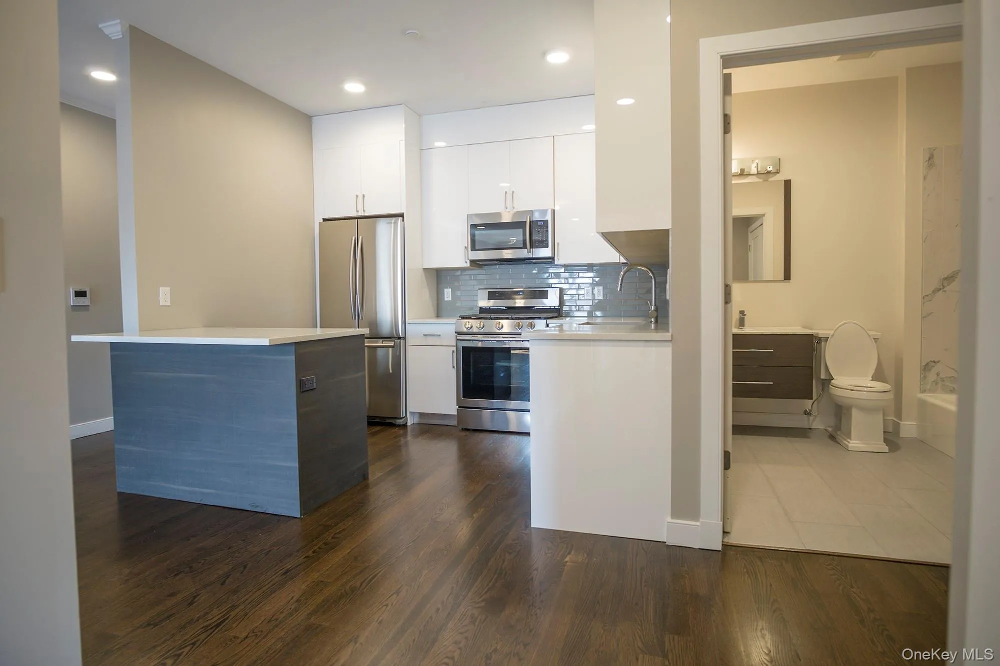 Kitchen with appliances with stainless steel finishes, white cabinetry, modern cabinets, dark wood-type flooring, and backsplash Kitchen with appliances with stainless steel finishes, white cabinetry, modern cabinets, dark wood-type flooring, and backsplash