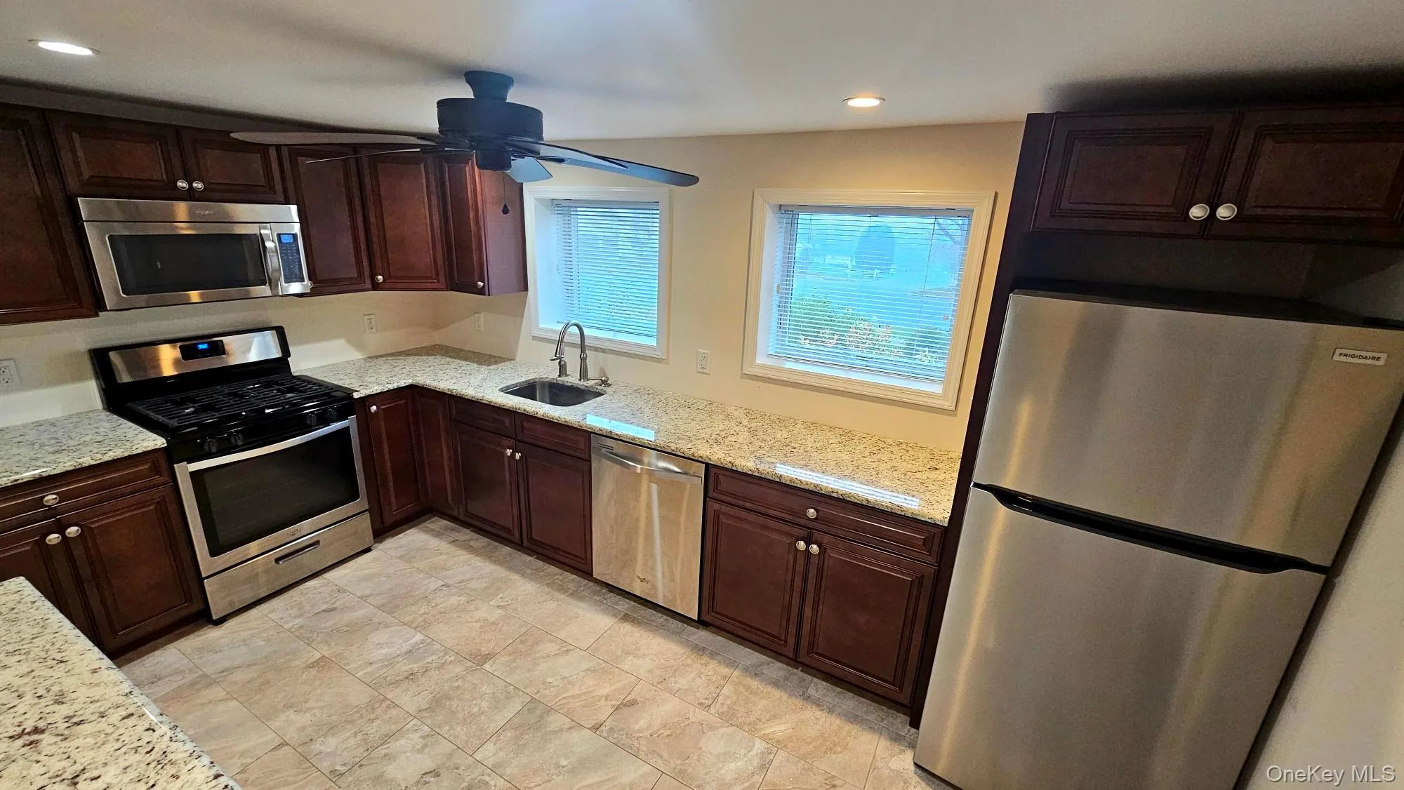 Kitchen with appliances with stainless steel finishes, dark brown cabinetry, light stone countertops, recessed lighting, and a ceiling fan Kitchen with appliances with stainless steel finishes, dark brown cabinetry, light stone countertops, recessed lighting, and a ceiling fan