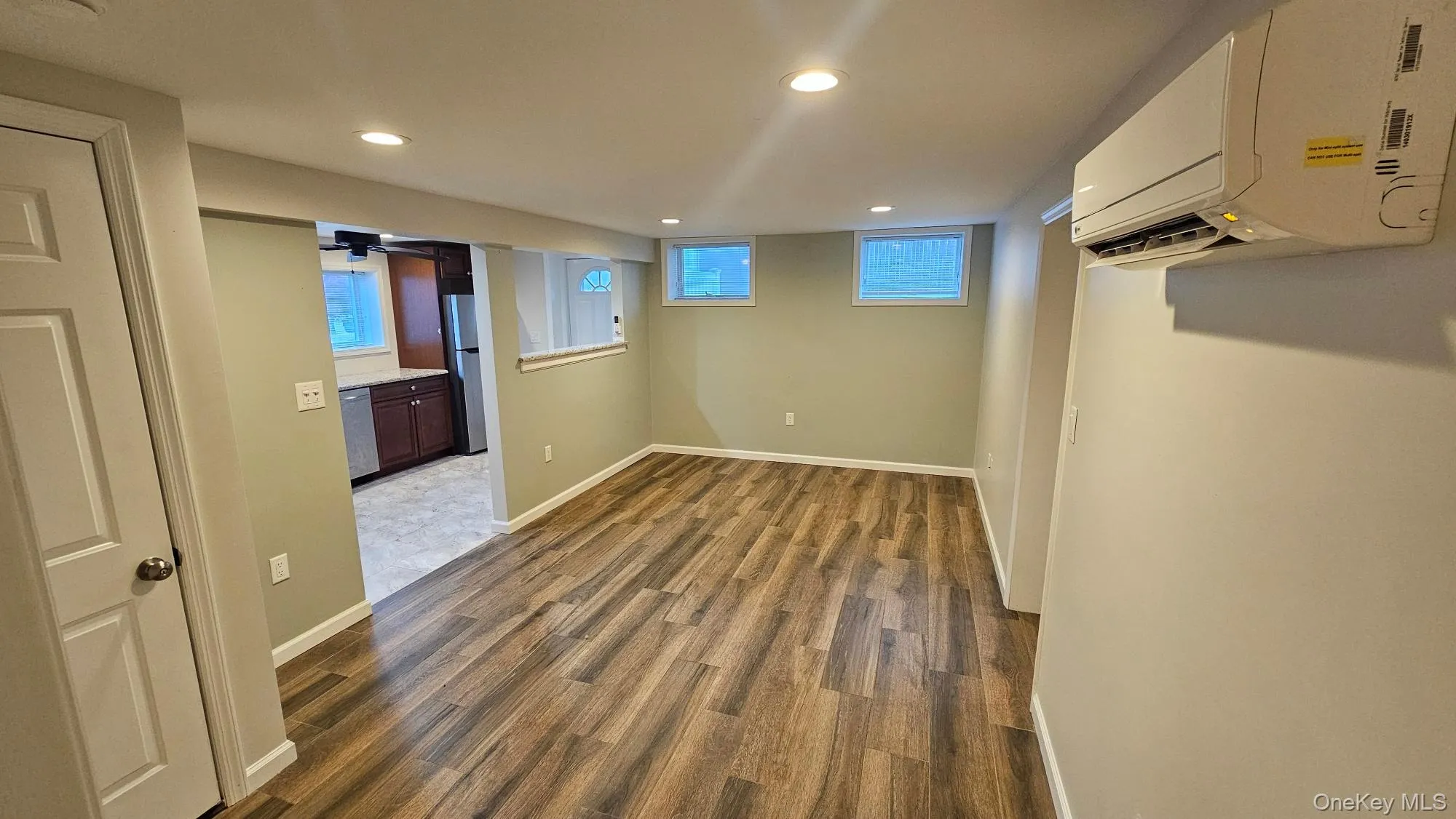 Below grade area featuring dark wood finished floors, recessed lighting, freestanding refrigerator, an AC wall unit, and ceiling fan Below grade area featuring dark wood finished floors, recessed lighting, freestanding refrigerator, an AC wall unit, and ceiling fan