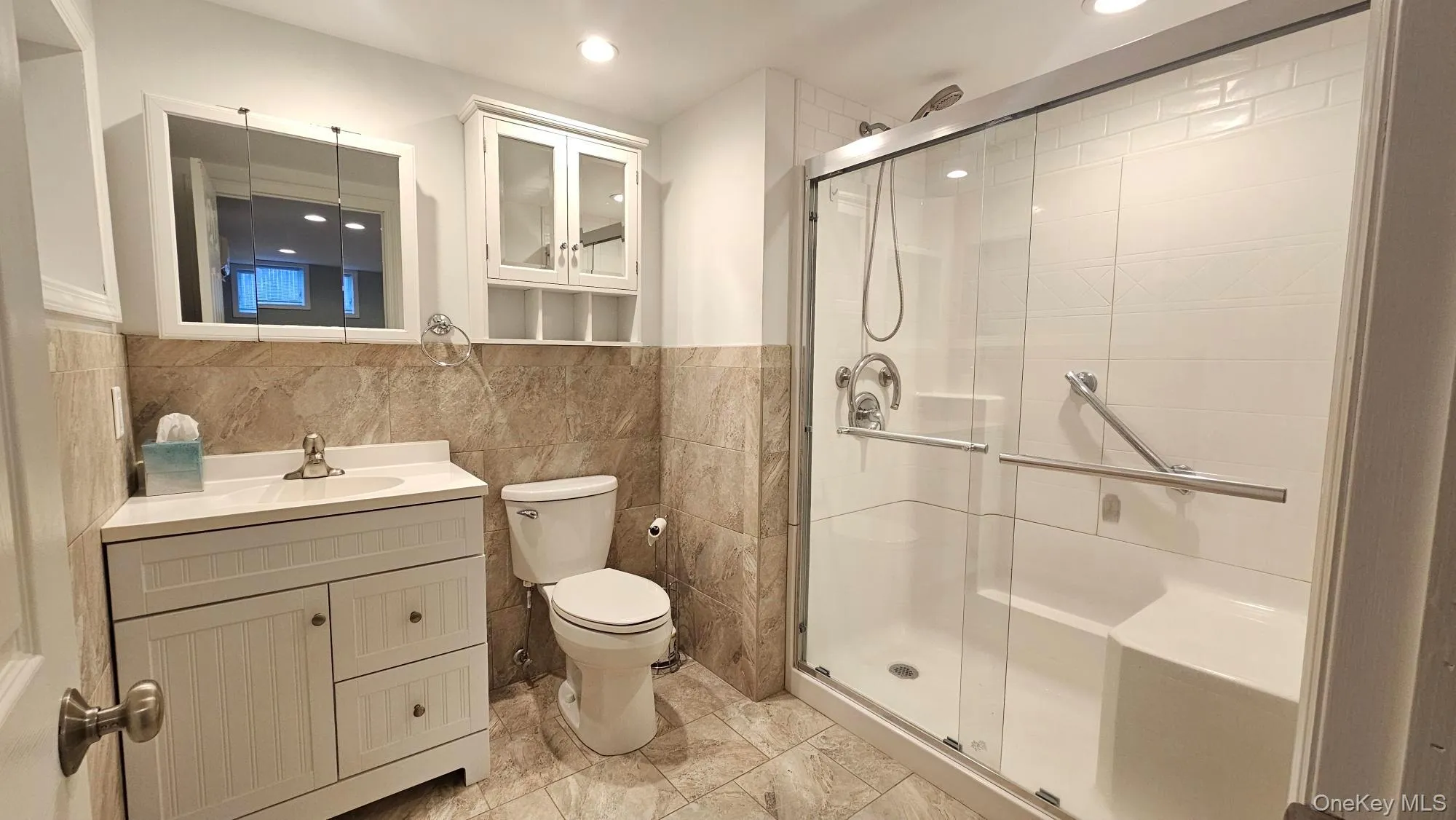 Bathroom with tile walls, vanity, a stall shower, a wainscoted wall, and recessed lighting Bathroom with tile walls, vanity, a stall shower, a wainscoted wall, and recessed lighting
