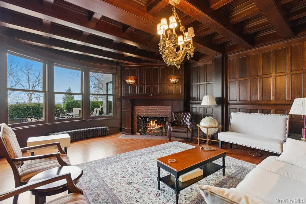 Parlor with wood millwork walls, a wood ceiling with exposed beams, brick fireplace, custom mermaid chandelier, and original oak floors Parlor with wood millwork walls, a wood ceiling with exposed beams, brick fireplace, custom mermaid chandelier, and original oak floors