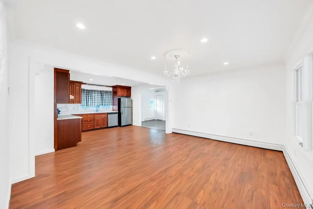 Unfurnished living room with a baseboard heating unit, dark wood-style flooring, recessed lighting, and a chandelier Unfurnished living room with a baseboard heating unit, dark wood-style flooring, recessed lighting, and a chandelier