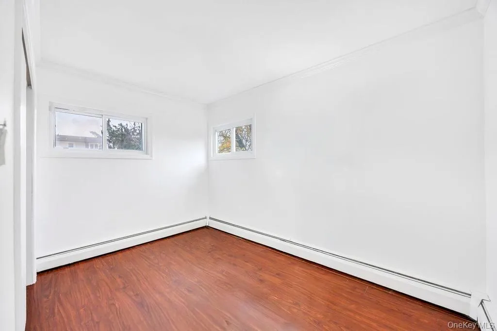 Unfurnished room with ornamental molding, baseboard heating, dark wood-style flooring, and a baseboard radiator Unfurnished room with ornamental molding, baseboard heating, dark wood-style flooring, and a baseboard radiator