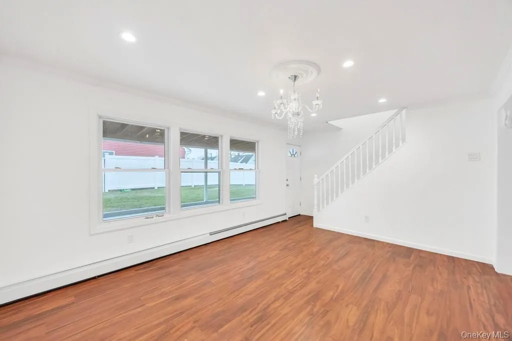 Unfurnished living room featuring a baseboard heating unit, ornamental molding, wood finished floors, stairs, and a chandelier Unfurnished living room featuring a baseboard heating unit, ornamental molding, wood finished floors, stairs, and a chandelier
