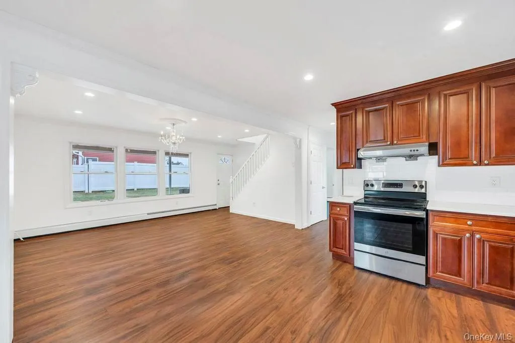 Kitchen with stainless steel range with electric stovetop, baseboard heating, dark wood-style floors, under cabinet range hood, and a chandelier Kitchen with stainless steel range with electric stovetop, baseboard heating, dark wood-style floors, under cabinet range hood, and a chandelier