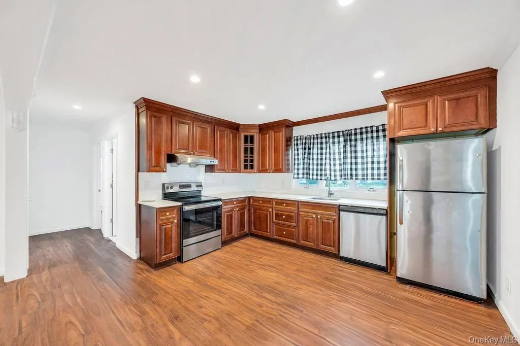 Kitchen featuring appliances with stainless steel finishes, light countertops, dark wood-type flooring, glass insert cabinets, and under cabinet range hood Kitchen featuring appliances with stainless steel finishes, light countertops, dark wood-type flooring, glass insert cabinets, and under cabinet range hood