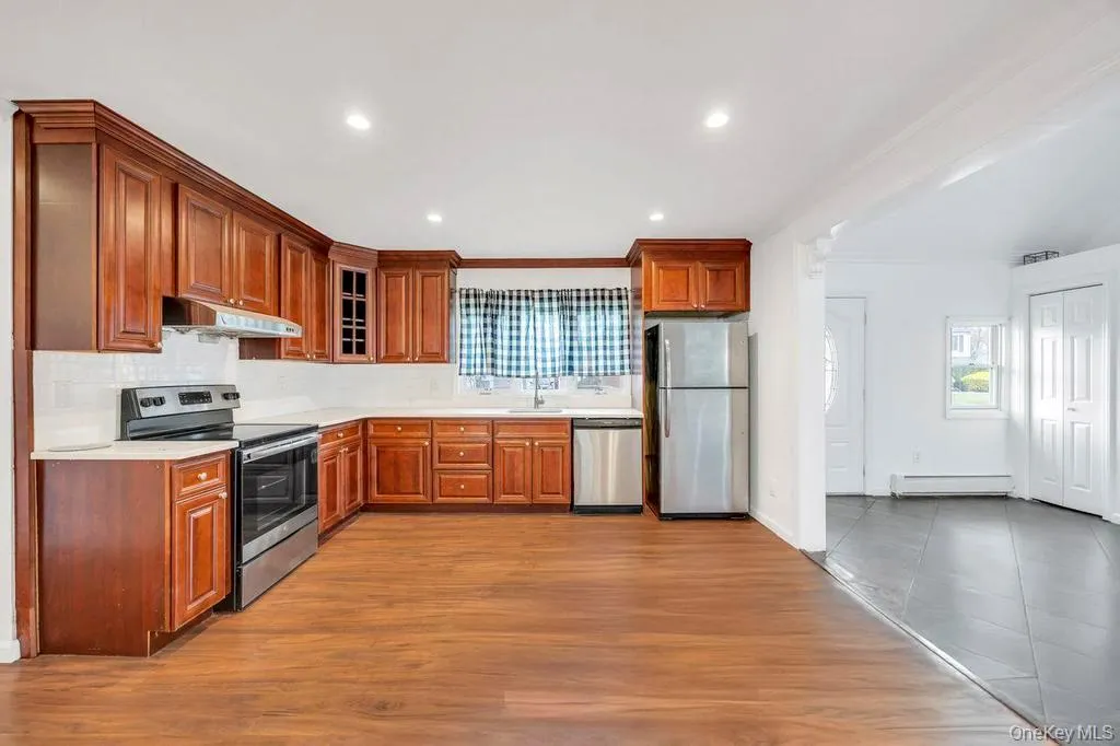 Kitchen featuring appliances with stainless steel finishes, light countertops, baseboard heating, under cabinet range hood, and dark wood finished floors Kitchen featuring appliances with stainless steel finishes, light countertops, baseboard heating, under cabinet range hood, and dark wood finished floors