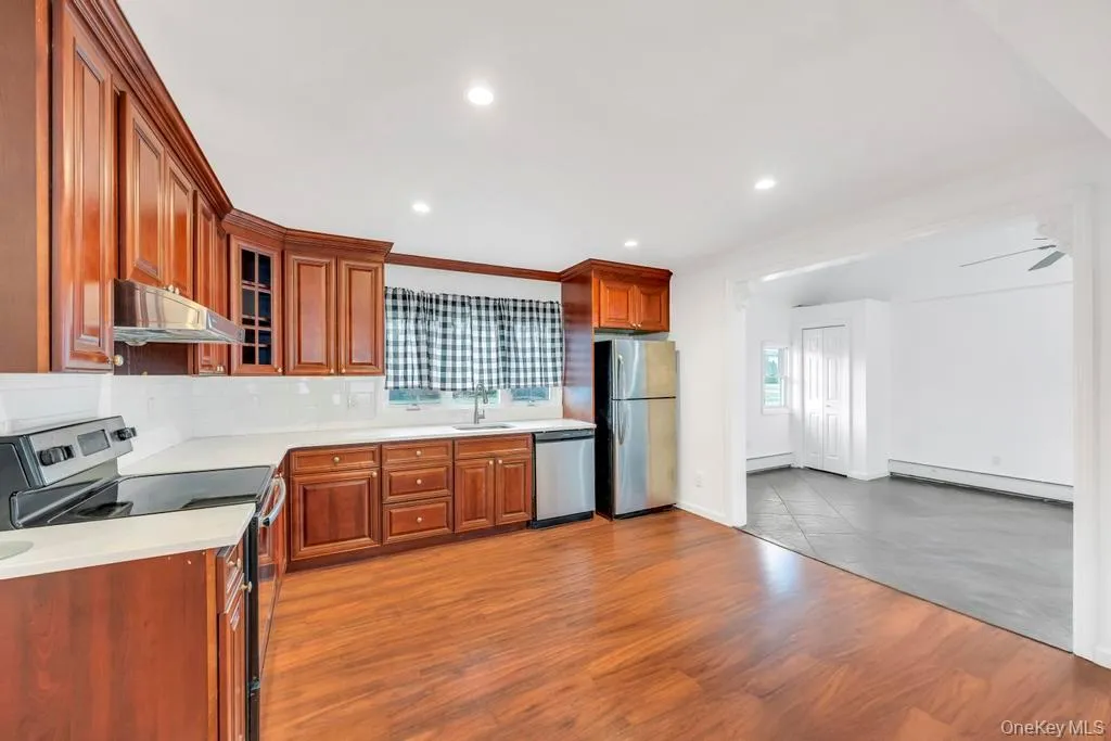 Kitchen with stainless steel appliances, glass insert cabinets, brown cabinetry, under cabinet range hood, and recessed lighting Kitchen with stainless steel appliances, glass insert cabinets, brown cabinetry, under cabinet range hood, and recessed lighting