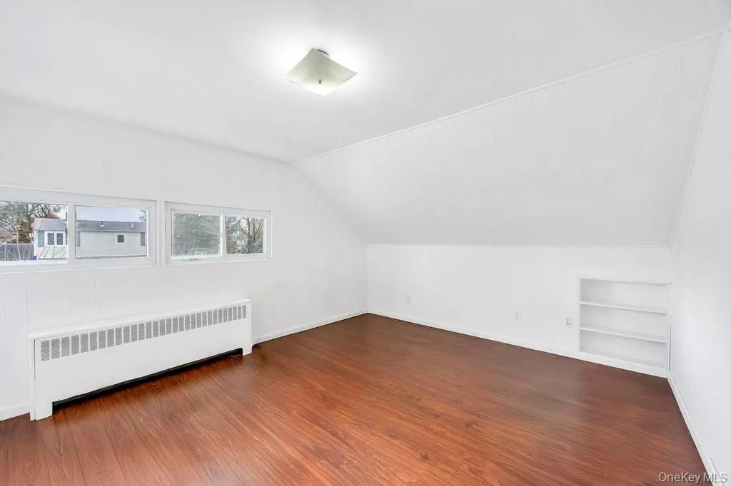Bonus room with radiator, built in shelves, dark wood-style floors, and vaulted ceiling Bonus room with radiator, built in shelves, dark wood-style floors, and vaulted ceiling