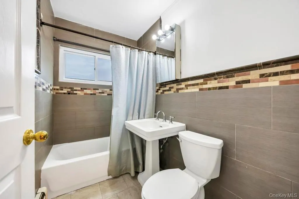 Full bath featuring shower / bathtub combination with curtain, tile walls, and a baseboard radiator Full bath featuring shower / bathtub combination with curtain, tile walls, and a baseboard radiator