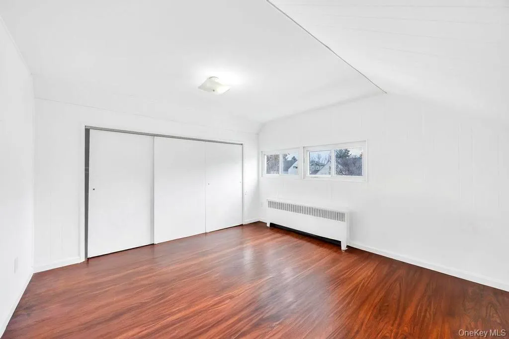 Unfurnished bedroom featuring radiator, dark wood-style flooring, vaulted ceiling, and a closet Unfurnished bedroom featuring radiator, dark wood-style flooring, vaulted ceiling, and a closet