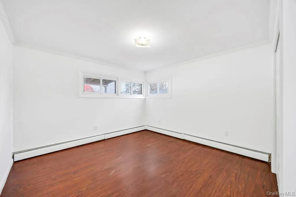 Empty room featuring dark wood-style flooring, a baseboard heating unit, crown molding, and a baseboard radiator Empty room featuring dark wood-style flooring, a baseboard heating unit, crown molding, and a baseboard radiator