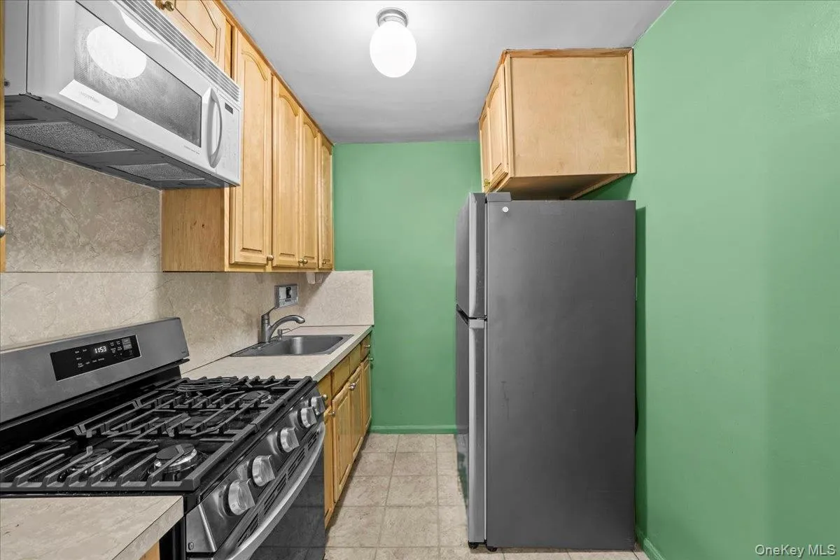 Kitchen featuring appliances with stainless steel finishes, backsplash, light countertops, light brown cabinets, and light tile patterned floors Kitchen featuring appliances with stainless steel finishes, backsplash, light countertops, light brown cabinets, and light tile patterned floors