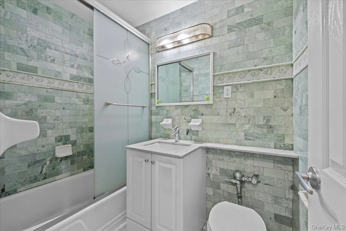 Full bath with vanity, tile walls, enclosed tub / shower combo, and decorative backsplash Full bath with vanity, tile walls, enclosed tub / shower combo, and decorative backsplash