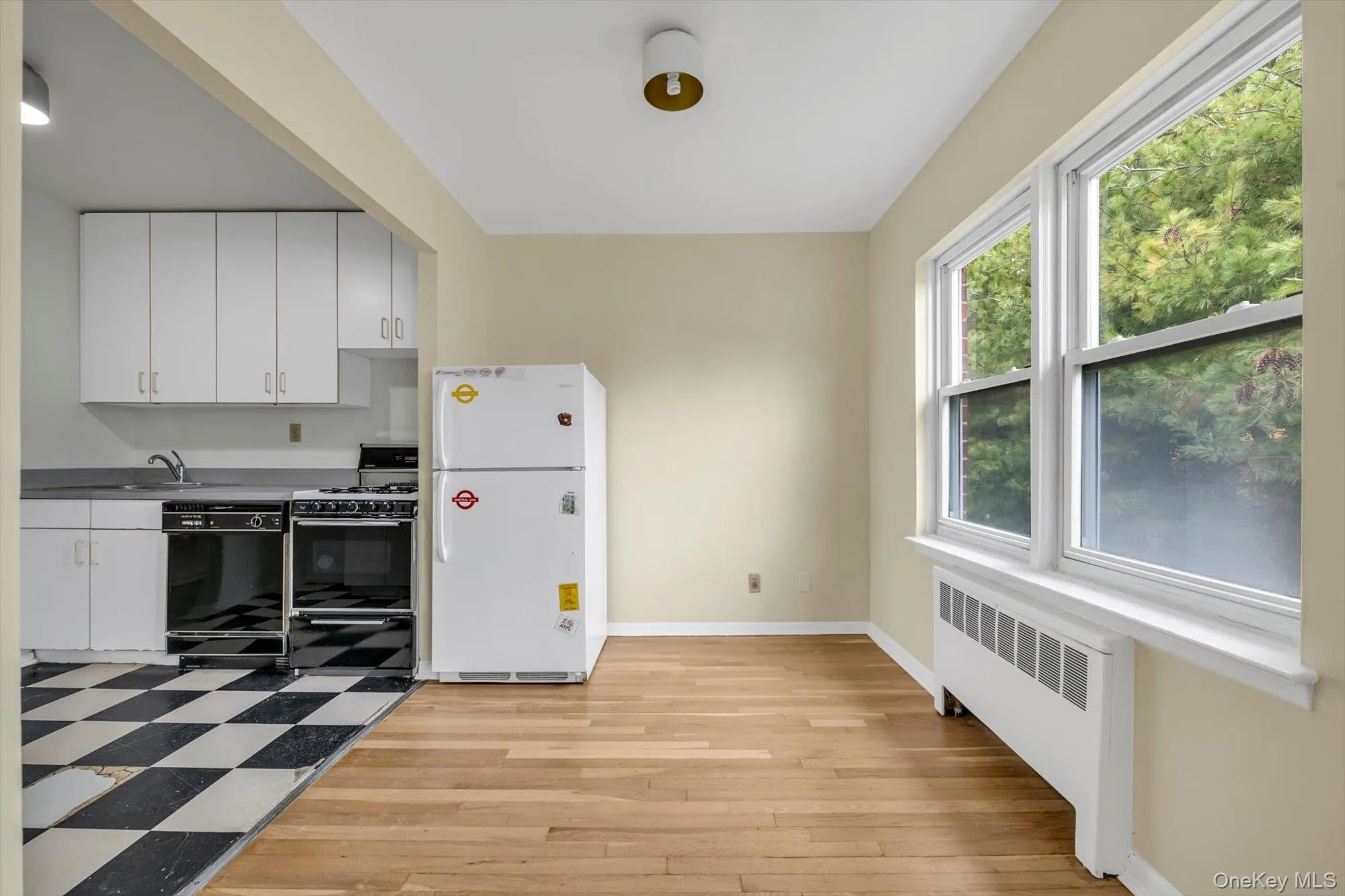 Kitchen featuring white cabinetry, black appliances, radiator heating unit, light wood-type flooring, and dark countertops Kitchen featuring white cabinetry, black appliances, radiator heating unit, light wood-type flooring, and dark countertops