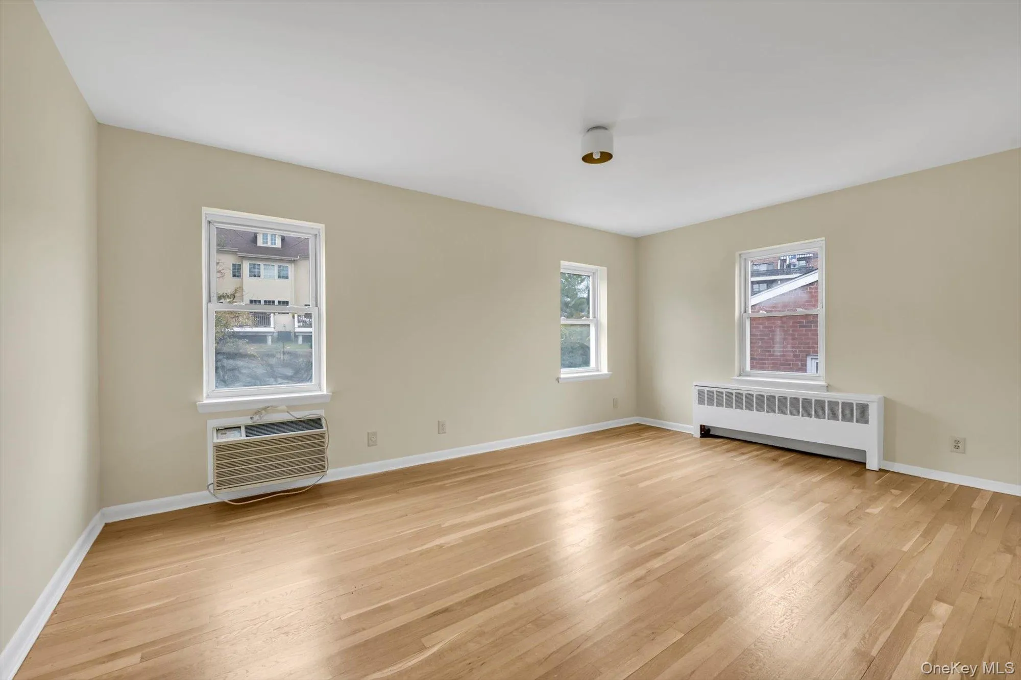 Empty room with radiator, light wood finished floors, and a wall unit AC Empty room with radiator, light wood finished floors, and a wall unit AC